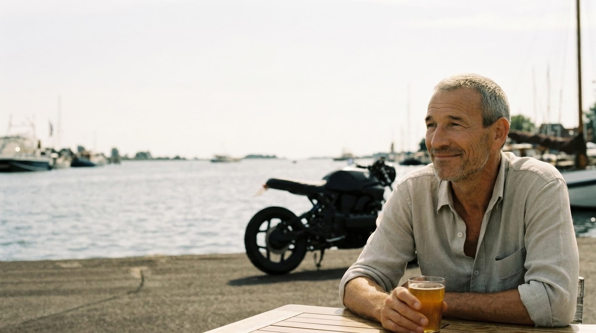Stimmungsbild: Peter auf einer Terrasse am Wasser, seine schwarze BMW K100 hinter ihm